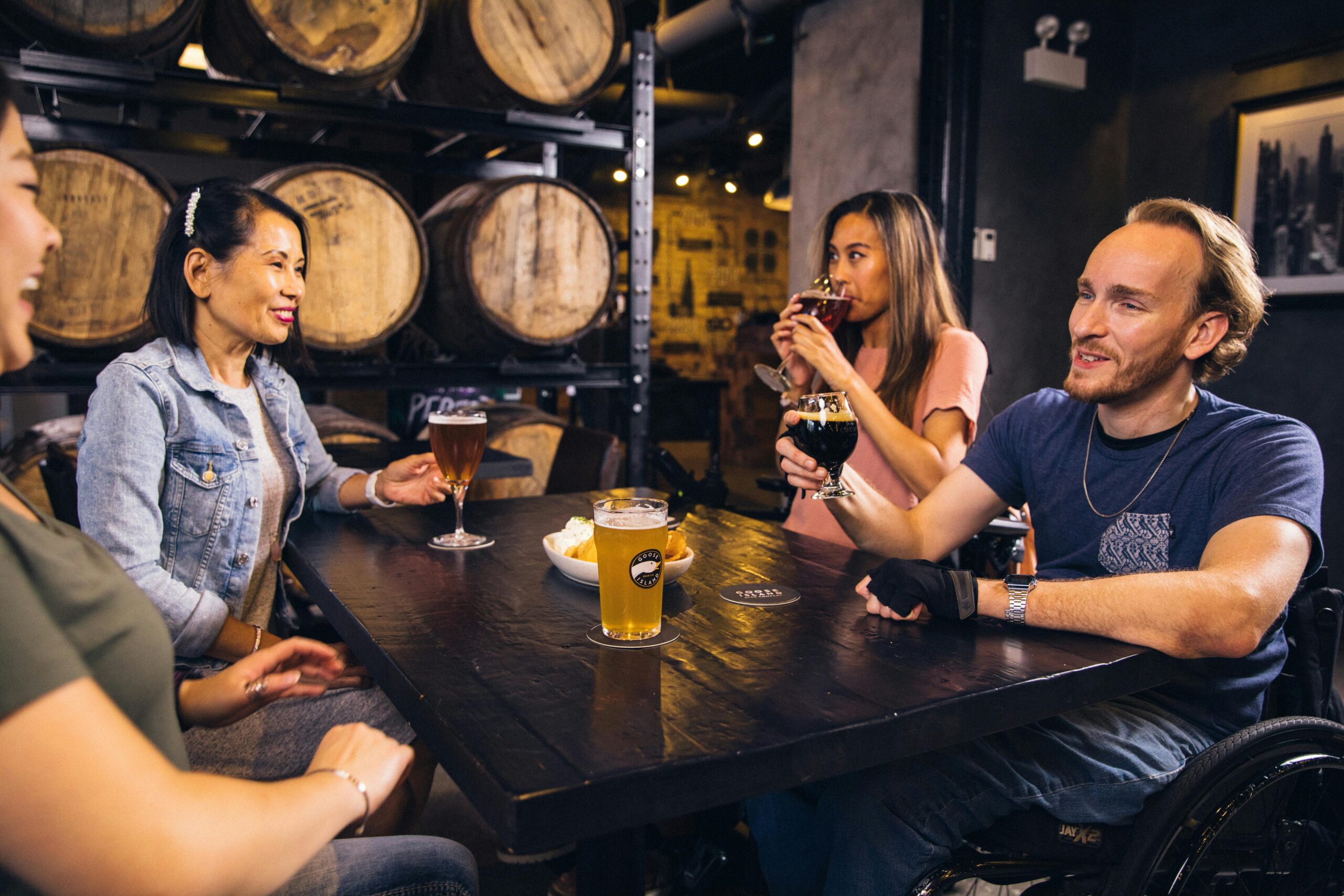 A diverse group of friends enjoying drinks and laughter at a cozy bar with wooden barrels.