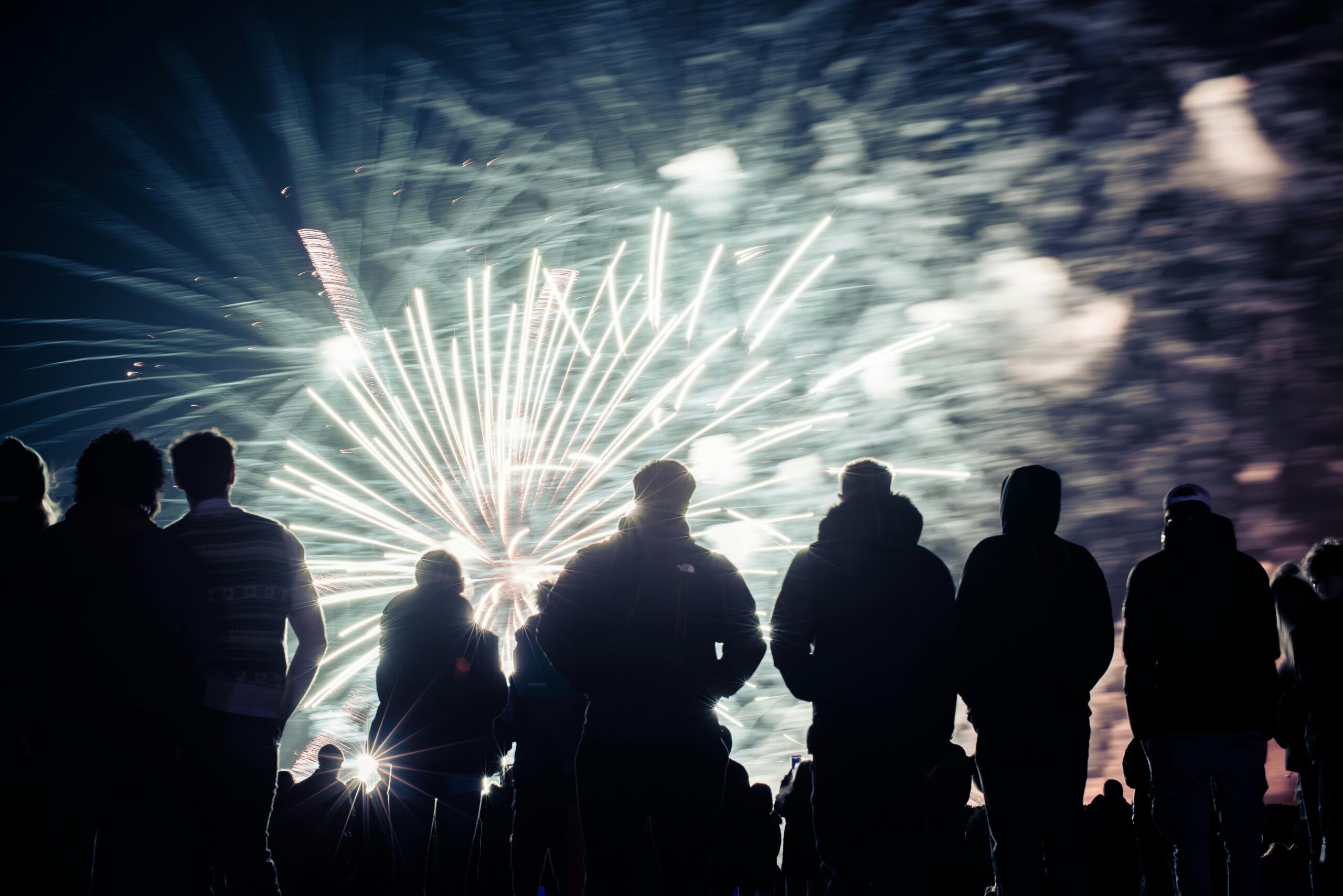 Silhouetted people enjoying a night fireworks show with vibrant lights in the sky.